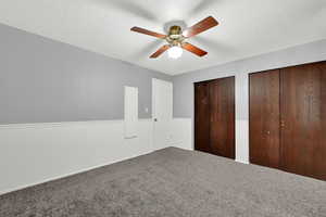 Unfurnished bedroom with two closets, ceiling fan, carpet, and a textured ceiling