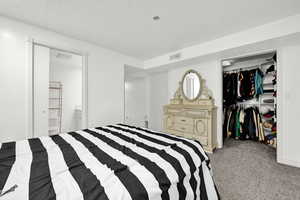 Carpeted bedroom with a textured ceiling, ensuite bathroom, and a closet