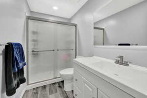 Bathroom featuring vanity, toilet, hardwood / wood-style floors, and a shower with door