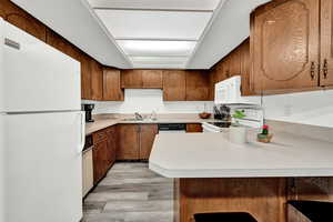 Kitchen featuring light wood-type flooring, white appliances, kitchen peninsula, and sink