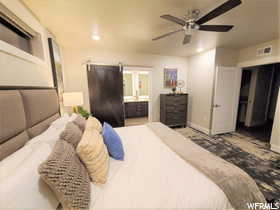 Bedroom featuring a barn door, ceiling fan, and connected bathroom