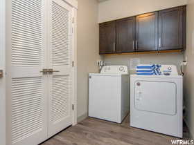 Laundry room with separate washer and dryer, cabinets, and light hardwood / wood-style floors