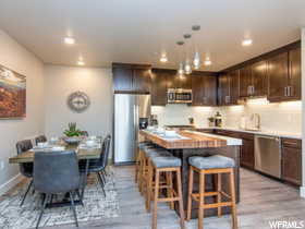 Kitchen with light wood-type flooring, dark brown cabinets, decorative light fixtures, a kitchen island, and appliances with stainless steel finishes