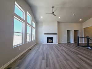 Unfurnished living room featuring a high ceiling, ceiling fan, wood-type flooring, and a brick fireplace