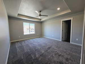 Carpeted empty room featuring a tray ceiling, a textured ceiling, and ceiling fan