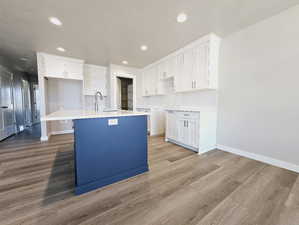 Kitchen featuring a kitchen island with sink, sink, decorative backsplash, white cabinetry, and light wood-type flooring