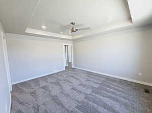 Carpeted spare room with a tray ceiling and ceiling fan