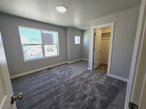 Unfurnished bedroom with dark carpet, a walk in closet, a closet, and multiple windows