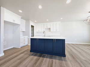 Kitchen with white cabinets, a center island with sink, and light hardwood / wood-style flooring