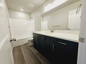 Full bathroom with vanity, toilet, washtub / shower combination, and hardwood / wood-style flooring