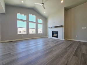 Unfurnished living room featuring high vaulted ceiling, a brick fireplace, hardwood / wood-style floors, and ceiling fan