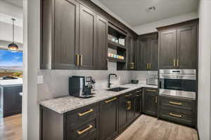 Kitchen with oven, light wood-type flooring, light stone counters, sink, and decorative backsplash