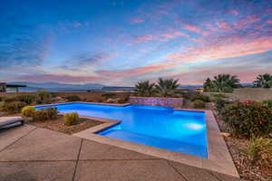 Pool at dusk featuring a mountain view and a patio area