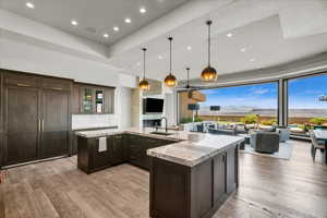 Kitchen with light wood-type flooring, light stone counters, decorative light fixtures, and dark brown cabinetry