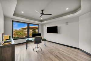 Home office with a tray ceiling, ceiling fan, and light hardwood / wood-style floors