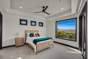 Bedroom with light carpet, a raised ceiling, and ceiling fan