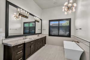 Bathroom with a bathing tub, a notable chandelier, vanity, lofted ceiling, and tile walls