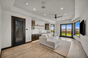 Living room with light wood-type flooring, a raised ceiling, and wet bar