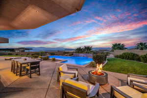 Patio terrace at dusk with a yard, a fenced in pool, a mountain view, and an outdoor living space with a fire pit