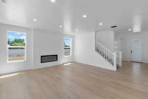 Unfurnished living room with light wood-type flooring, a large fireplace, and plenty of natural light