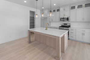 Kitchen with a kitchen island with sink, white cabinetry, stainless steel appliances, sink, and light hardwood / wood-style floors