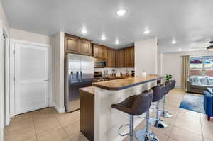 Kitchen featuring a kitchen bar, light tile patterned floors, kitchen peninsula, ceiling fan, and appliances with stainless steel finishes