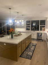 Kitchen with light wood-type flooring, a kitchen island, decorative light fixtures, and white cabinets