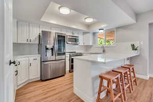 Kitchen featuring stainless steel appliances, a kitchen breakfast bar, kitchen peninsula, and white cabinets