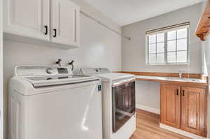 Laundry area with light wood-type flooring, washing machine and clothes dryer, cabinets, and sink