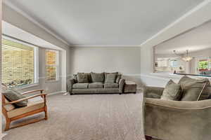 Living room with ornamental molding, an inviting chandelier, and carpet floors