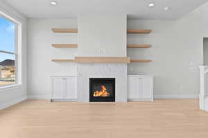 Unfurnished living room featuring light wood-style floors, a premium fireplace, baseboards, and recessed lighting