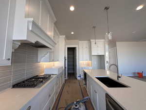 Kitchen featuring hanging light fixtures, white cabinets, light stone countertops, and sink