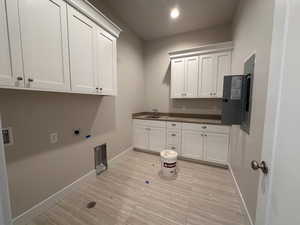 Clothes washing area with sink, electric dryer hookup, and cabinets