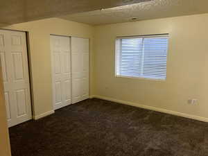 Unfurnished bedroom with baseboards, a textured ceiling, and dark colored carpet