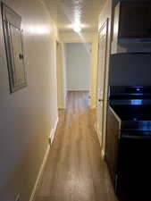Corridor featuring baseboards, a textured ceiling, electric panel, and light wood-type flooring