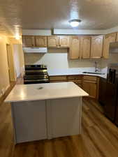 Kitchen featuring light countertops, dark wood-style flooring, stainless steel appliances, under cabinet range hood, and a sink
