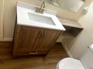Half bath with baseboards, toilet, vanity, and wood finished floors