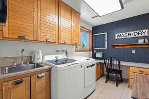 Washroom featuring light tile patterned floors, sink, washer and dryer, wood walls, and cabinets