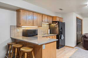 Kitchen featuring light wood-type flooring, sink, black appliances, kitchen peninsula, and decorative backsplash