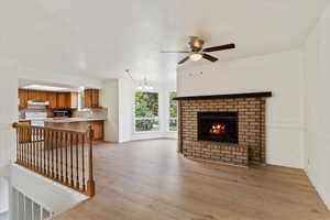 Living room featuring ceiling fan with notable chandelier, sink, a fireplace, and light hardwood / wood-style floors