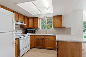 Kitchen with decorative backsplash, white appliances, kitchen peninsula, light wood-type flooring, and sink