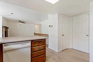 Kitchen featuring ceiling fan, white dishwasher, light hardwood / wood-style flooring, and a fireplace