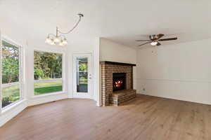 Unfurnished living room with a brick fireplace, ceiling fan with notable chandelier, and light wood-type flooring