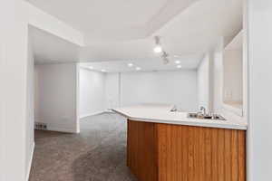 Kitchen with track lighting, sink, dark colored carpet, and kitchen peninsula