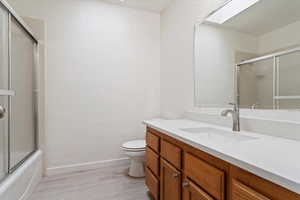 Full bathroom with a skylight, vanity, hardwood / wood-style flooring, combined bath / shower with glass door, and toilet