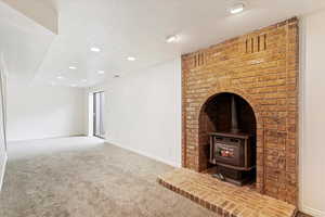 Unfurnished living room with a textured ceiling, carpet, and a wood stove