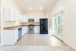 Kitchen featuring appliances with stainless steel finishes, light tile patterned floors, white cabinetry, and vaulted ceiling