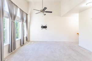 Unfurnished room featuring a towering ceiling, light colored carpet, and ceiling fan