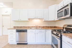 Kitchen featuring appliances with stainless steel finishes, light tile patterned floors, white cabinetry, and sink