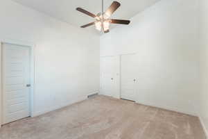 Interior space featuring a towering ceiling, light colored carpet, and ceiling fan